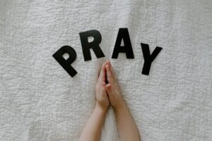 Close-up of hands in prayer on white quilted fabric with PRAY letters.